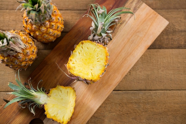 Sovraccarico di ananas diviso in due sul tagliere sulla tavola di legno