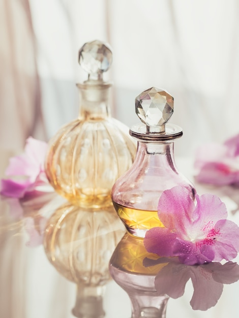 Spa ancora in vita con bottiglie di profumo e oli aromatici circondate da fiori, sulla superficie chiara