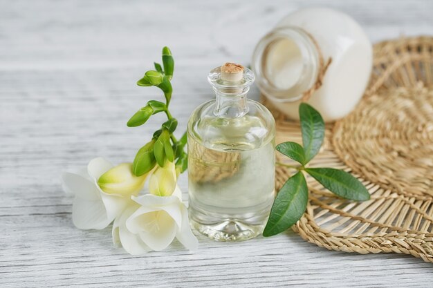 Spa ancora in vita con profumo e bottiglia di olio aromatico circondato da fiori di fresia, sulla superficie chiara