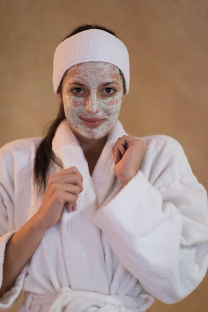 Spa Donna che applica maschera facciale Trattamenti di bellezza Primo piano ritratto di bella ragazza con un asciugamano sulla testa che applica maschera facciale