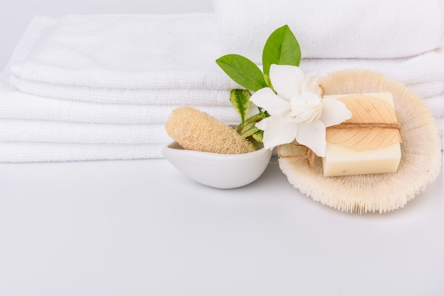 Spa e concetti sanitari impostati con una pila di asciugamani bianchi e fiori tropicali Gardenia latte sapone luffa scrub su sfondo bianco