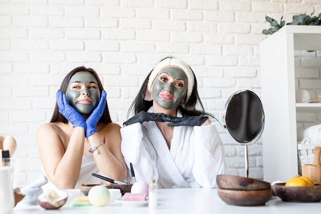 Spa e concetto di benessere. Automedicazione. Due belle donne in guanti che applicano la maschera facciale divertendosi