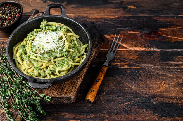 Spaghetti al pesto, spinaci e parmigiano in padella. Sfondo in legno scuro. Vista dall'alto. Copia spazio.