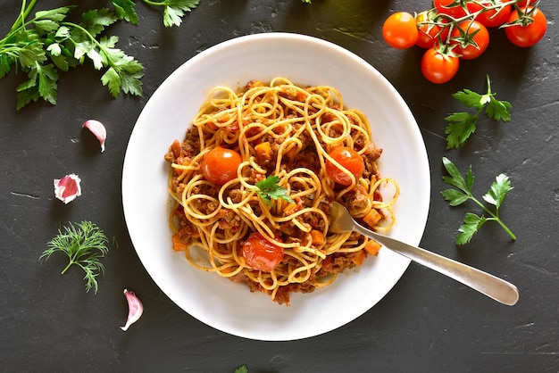 Spaghetti alla bolognese con carne macinata pomodorini su tavola di pietra nera Vista dall'alto piatto