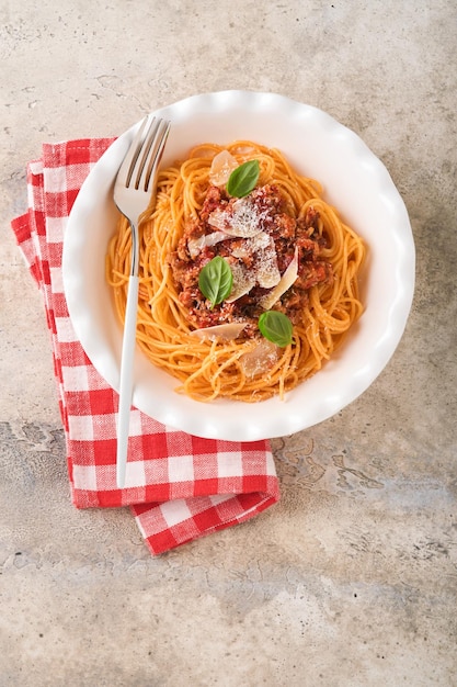 Spaghetti alla bolognese Gustosi spaghetti italiani appetitosi con salsa alla bolognese salsa di pomodoro formaggio parmigiano e basilico su piatto bianco su pietra grigia o cemento sullo sfondo del tavolo Vista dall'alto