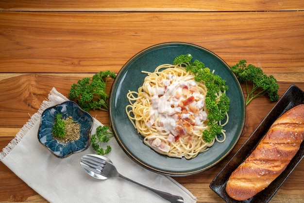 Spaghetti alla carbonara con prosciutto e pancetta sulla zolla verde sulla tavola di legno