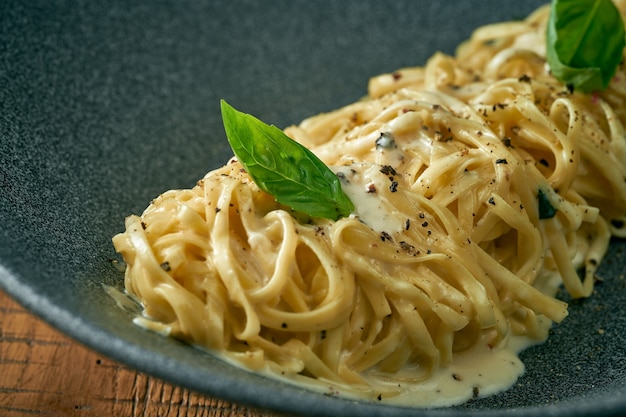 Spaghetti cacho pepe in un piatto grigio su uno sfondo di legno. pasta cremosa