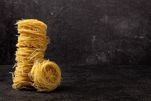 Spaghetti capellini su uno sfondo scuro strutturale con spazio da copiare. Spaghetti impilati in una torre