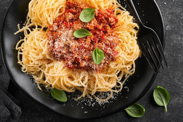 Spaghetti classici alla bolognese Gustosi spaghetti italiani appetitosi con salsa alla bolognese salsa di pomodoro formaggio parmigiano e basilico su piatto nero su pietra ardesia scura o sfondo tavolo in cemento