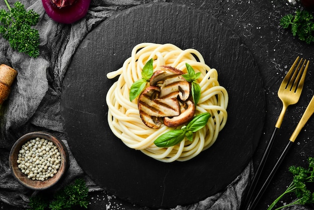 Spaghetti con funghi e basilico in una lastra di pietra nera Cibo italiano Vista dall'alto Spazio libero per il testo