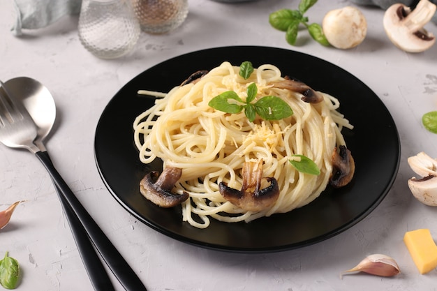 Spaghetti con funghi e basilico sulla banda nera su uno sfondo grigio