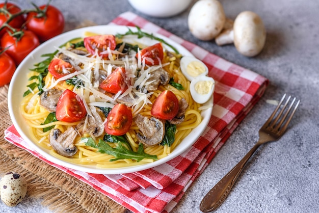 Spaghetti con funghi, formaggio, spinaci, rukkola e pomodorini. Piatto italiano, cultura mediterranea