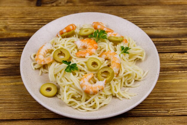 Spaghetti con gamberi olive verdi e prezzemolo su tavola di legno