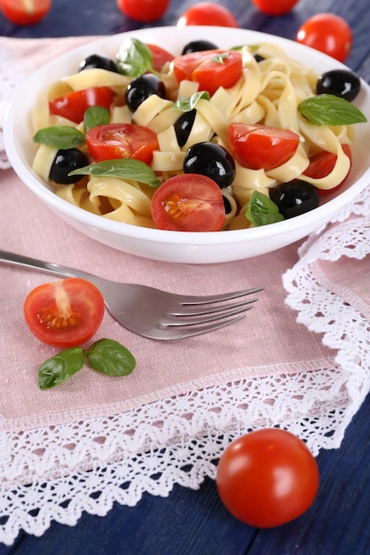 Spaghetti con pomodori, olive e foglie di basilico sul piatto sul tovagliolo di pizzo rosa su fondo di legno