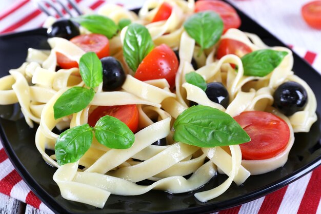 Spaghetti con pomodori olive e foglie di basilico sulla banda nera sul tovagliolo sulla tavola di legno