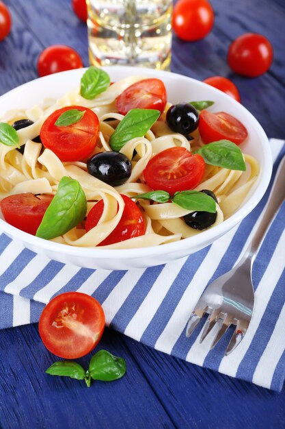 Spaghetti con pomodori, olive e foglie di basilico sulla piastra sul tovagliolo sulla tavola di legno