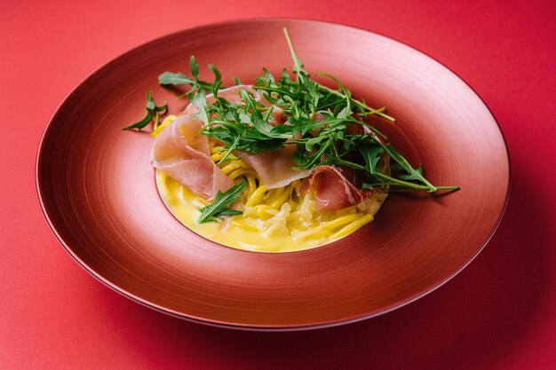 Spaghetti con prosciutto e rucola su piatto rosso