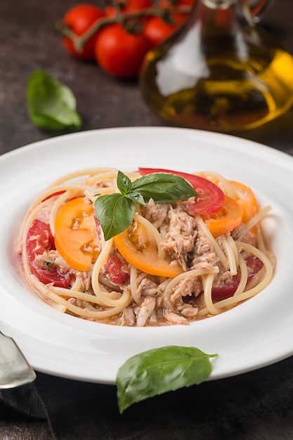 Spaghetti con tonno e salsa di aglio sulla piastra bianca su sfondo scuro