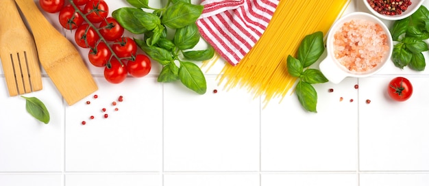 Spaghetti crudi con parmigiano e pomodori, basilico, aglio e olio sulla parete leggera con pepe sulla parete del tavolo bianco. Ingredienti tradizionali per la preparazione della pasta italiana. Vista dall'alto.