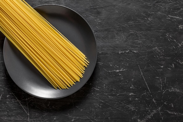 Spaghetti crudi, pasta italiana lunga, su sfondo scuro vista dall'alto piatto grigio, con spazio per copiare il testo.