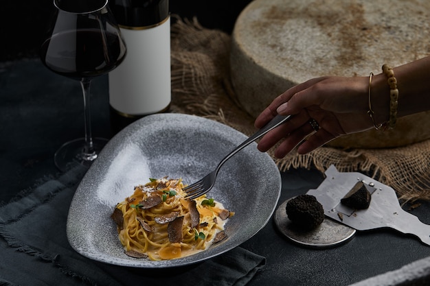 Spaghetti della cucina italiana con tartufo nero su un piatto grigio e una bottiglia di vino Messa a fuoco selettiva Verticale