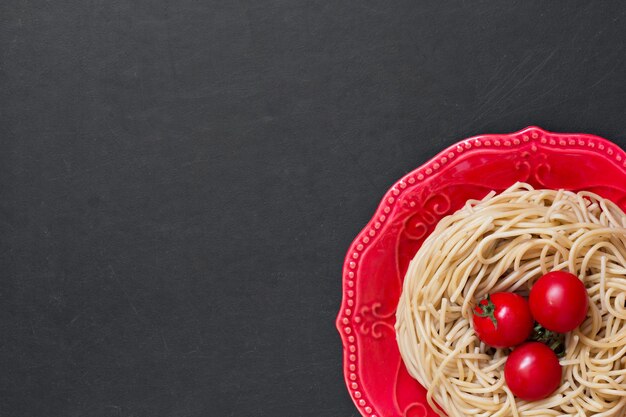 Spaghetti di grano duro vista dall'alto su piatto rosso su sfondo nero