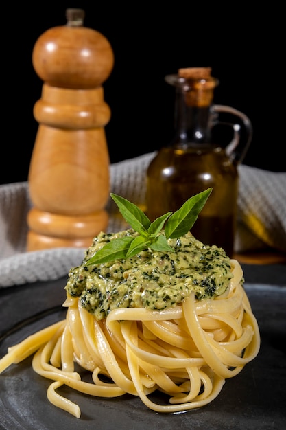 Spaghetti di pasta al pesto e foglie di basilico fresco in banda nera.