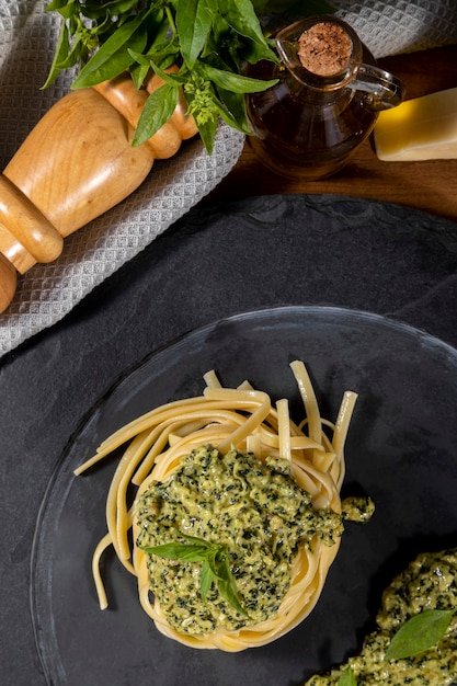 Spaghetti di pasta al pesto e foglie di basilico fresco in piatto di pietra nera su fondo di legno.