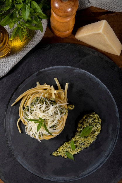 Spaghetti di pasta al pesto e foglie di basilico fresco in piatto di pietra nera su fondo di legno.