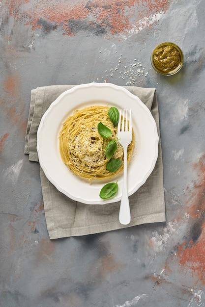 Spaghetti di pasta al pesto e foglie di basilico fresco in una ciotola bianca.