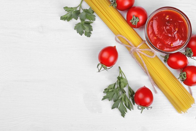 Spaghetti di pasta con pomodorini, salsa rossa e prezzemolo su fondo di legno bianco.