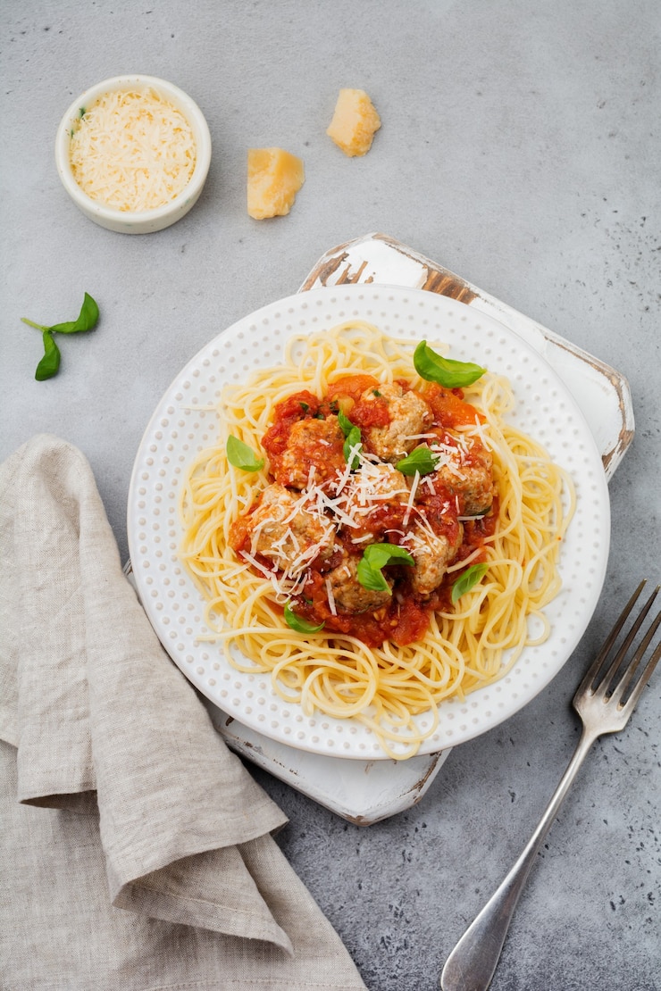 Foto spaghetti di pasta con salsa di pomodoro, parmigiano, basilico e polpette di carne sul piatto in ceramica bianca su cemento grigio o sfondo di pietra