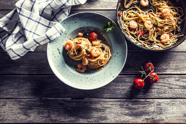 Spaghetti di pasta su piatto e padella con salsa di pomodoro gamberetti pomodori ed erbe aromatiche. Cucina italiana o mediterranea.