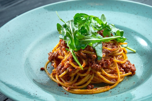 Spaghetti di pasta tradizionale con carne macinata e ragù di pomodoro con rucola, serviti in un piatto blu su una superficie di legno nera. cucina italiana