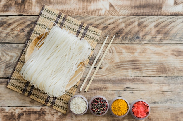 Spaghetti di riso crudo con le bacchette e ciotole di spezie secche sul tavolo