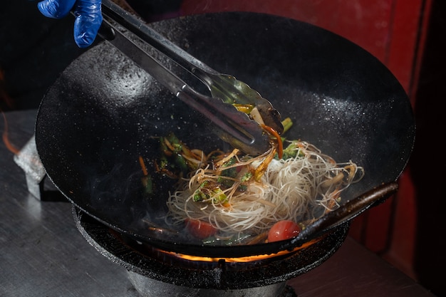 Spaghetti di riso flambe di Funchoza con verdure che cuociono sul fuoco in padella wok. Cibo di strada.