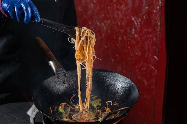 Spaghetti di riso flambe di Funchoza con verdure che cuociono sul fuoco in padella wok. Cibo di strada.