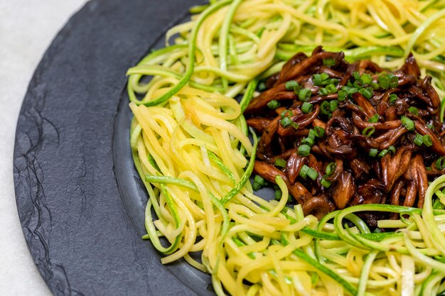 Spaghetti di zucchine con shimeji su lastra di pietra nera.