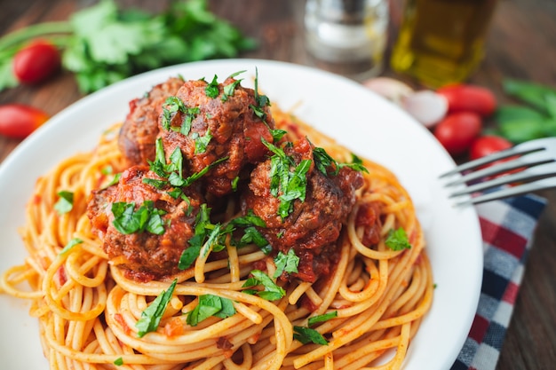 Spaghetti e polpette con salsa di pomodoro in piatto bianco sul bordo rustico in legno