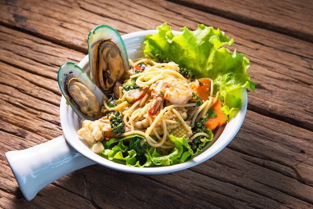 Spaghetti fritti piccanti con frutti di mare, metti in una bella tazza di terracotta, metti su un tavolo di legno.