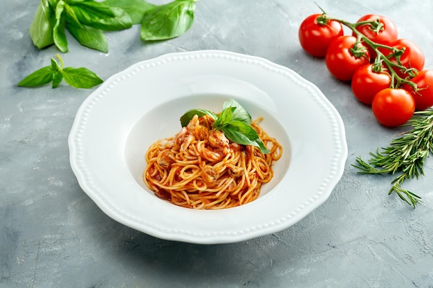 Spaghetti italiani con pomodori e gamberi in un piatto bianco su sfondo grigio