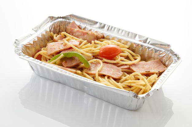 Spaghetti nella consegna dell&#39;alimento della scatola dello stagnola sul fondo di bianco della tavola