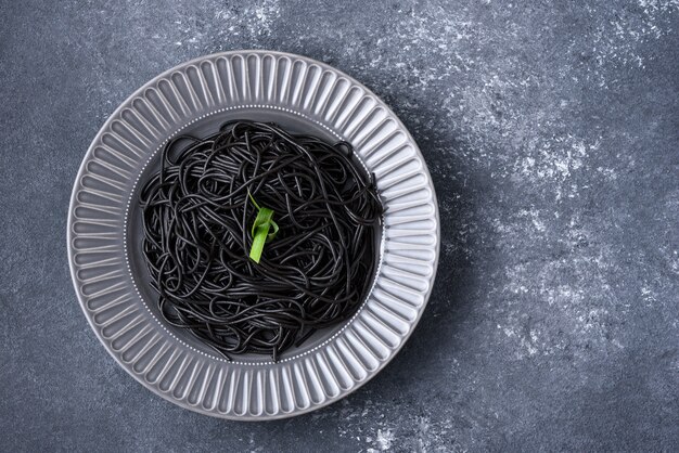 Spaghetti neri al nero di seppia con foglia verde su lastra grigia su sfondo grigio con copia spazio, concetto di pasta nera