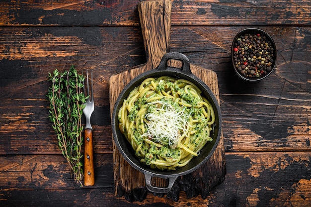 Spaghetti Pasta al pesto, spinaci e parmigiano in padella. Fondo di legno scuro. Vista dall'alto.