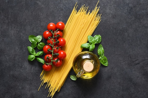 Spaghetti, pomodori e basilico su una superficie di cemento nero.