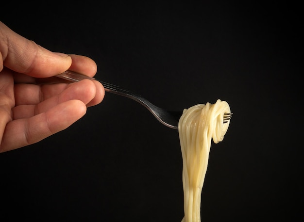 Spaghetti su una forchetta di metallo in mano a una persona Concetto di cibo con spazio per ricette o menu su sfondo nero