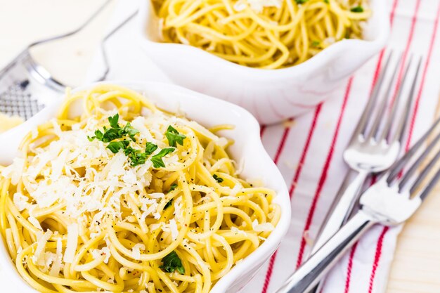 Spaghetty al formaggio e pepe con contorno verde in ciotole bianche.