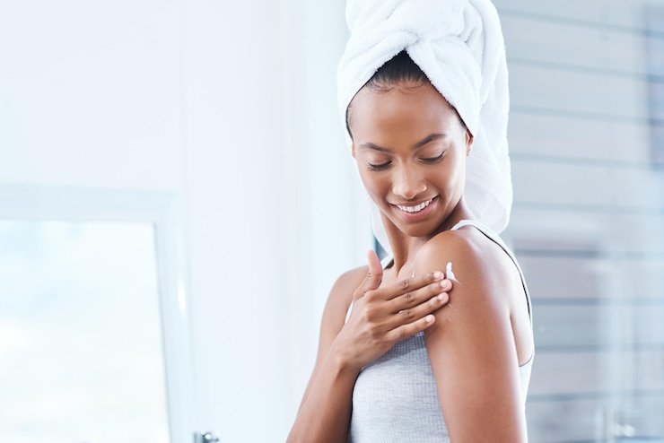 Foto spalla donna felice e crema per il corpo per la cura della pelle in bagno o casa per l'idratazione luce o lucentezza naturale lozione sorriso e persona femminile con cosmetici asciugamano e vitamina c per i risultati di bellezza