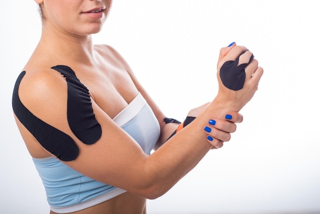 Spalla femminile con kineziotape su sfondo bianco Medicina alternativa per infortuni sportivi di articolazioni e legamenti Sportiva con una cartella clinica nera su una spalla dolorante e un dito medio