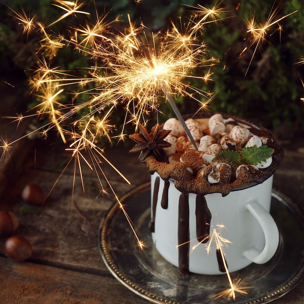 Sparkler di Natale in tazza bianca di cioccolata calda con marshmallow e cannella su un piatto d'epoca